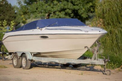 a white boat with a blue tarp covering the top, sitting on a boat trailer on land