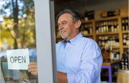 older man flipping sign in store window to 'open'