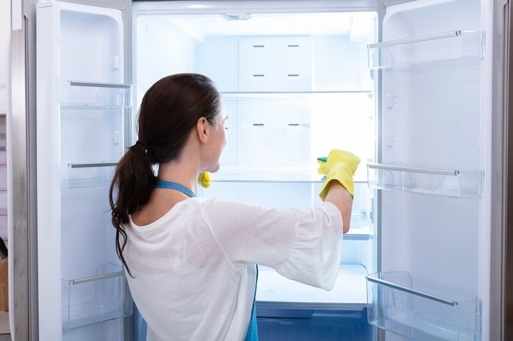 A woman wearing rubber gloves scrubbing the interior of her refrigerator.