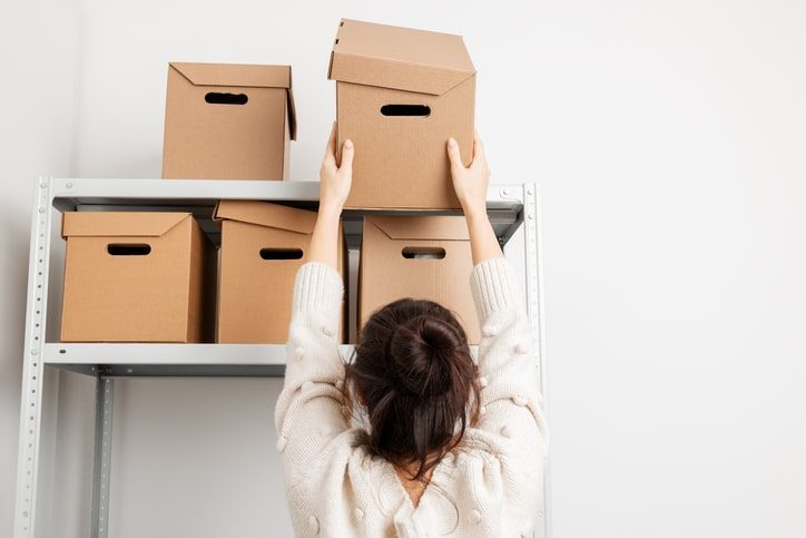 A woman placing boxes on a storage unit’s shelving.