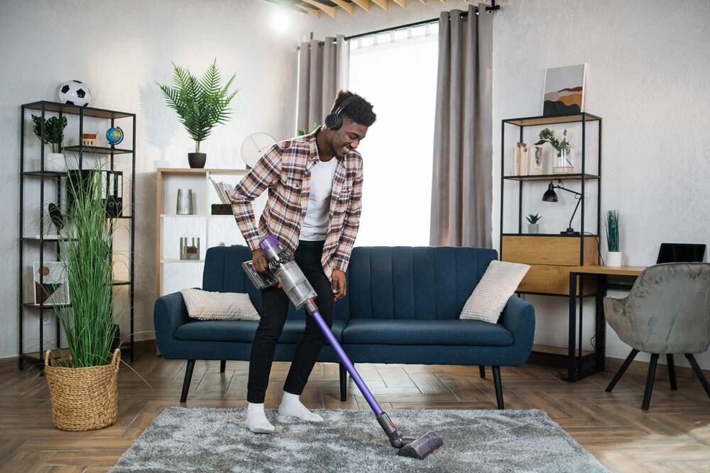 Young guy enjoying housekeeping using vaccuum cleaner and listening to music