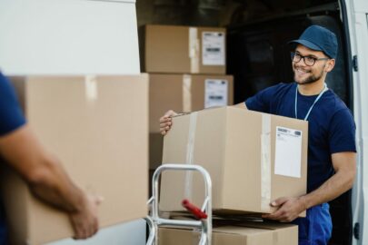 Young happy delivery man unloading boxes from a mini van