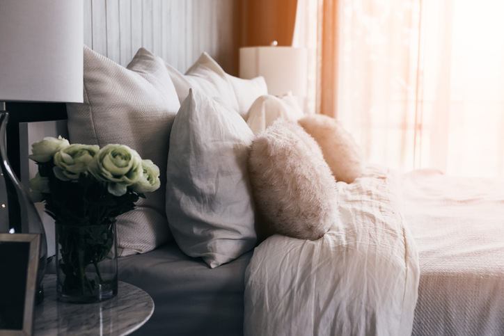 A cozy bed with fluffy pillows, linens, and flowers on a bedside table.