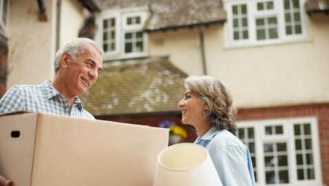 Couple outside a large home with a box and a lamp.