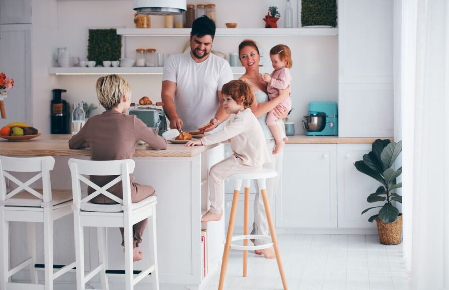 A happy family with three kids having breakfast in the kitchen in the morning.