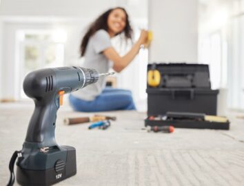 A close-up of a power drill with a woman in the background.